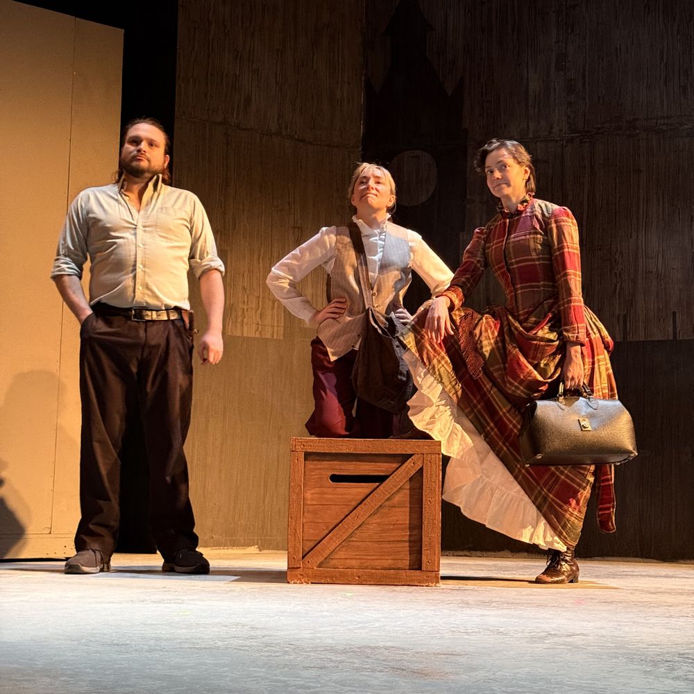 Three actors rehearsing on stage under warm theatrical light